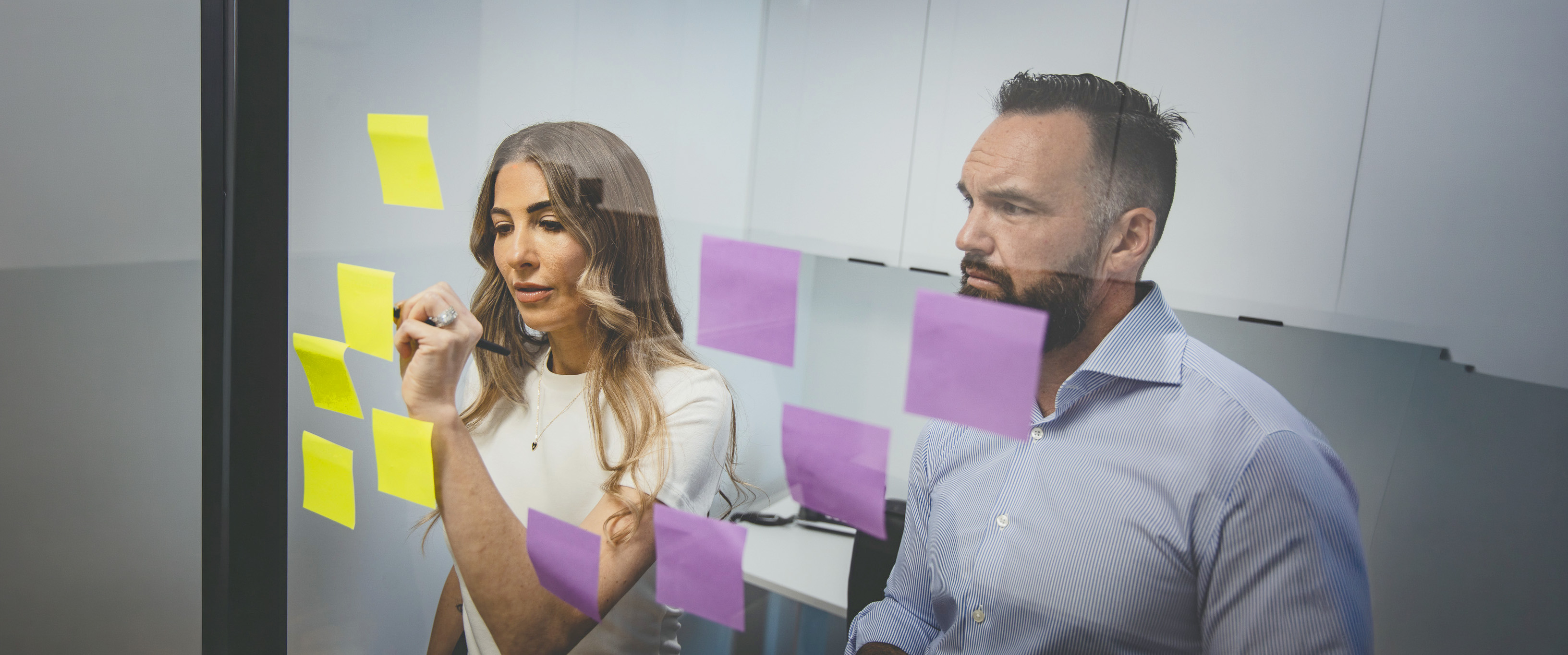 Colleagues mapping ideas on a glass sticky-note wall