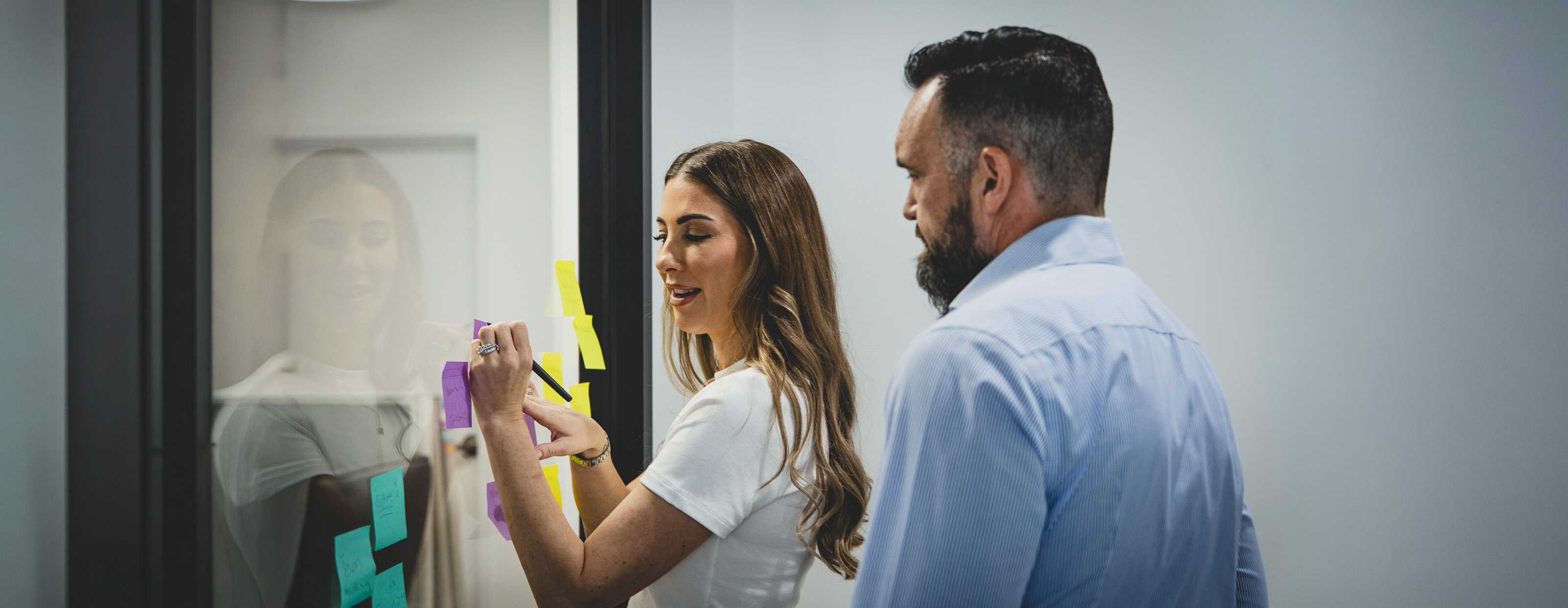 A facilitator writing on a glass sticky-note wall